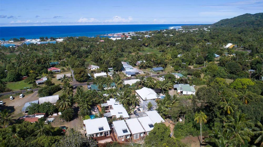 Aerial view of a tropical coastal village surrounded by dense greenery, with the ocean in the background, showcasing lush landscapes and seaside living.
