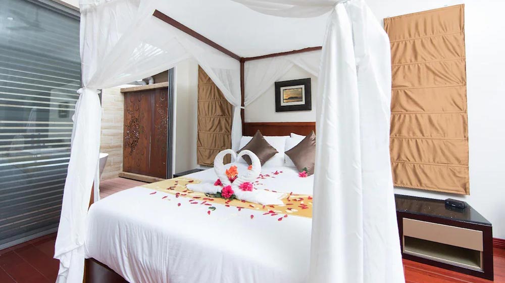 Elegant bedroom with canopied bed, romantic towel swans, and tropical decor, perfect for a relaxing getaway at Deepblue home. Ideal for romantic vacations and vacation rentals.