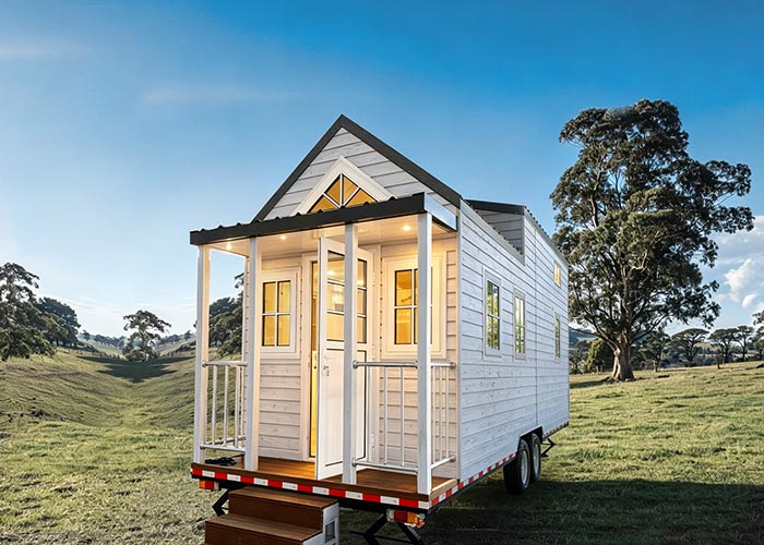 Portable tiny house on wheels featuring white exterior siding, a small front porch, and large windows, ideal for compact living and mobility.