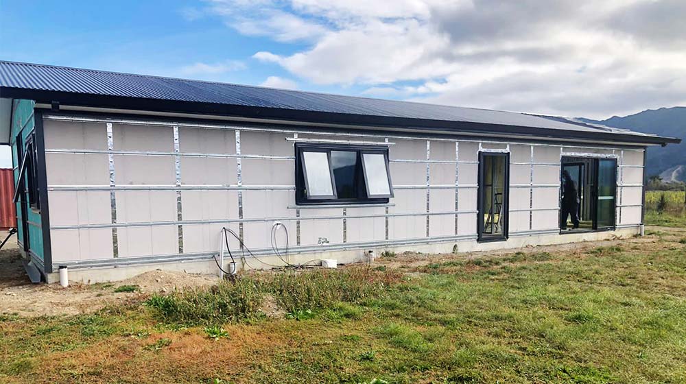 Modern prefab tiny house with metal siding and black-framed windows in a scenic outdoor setting.