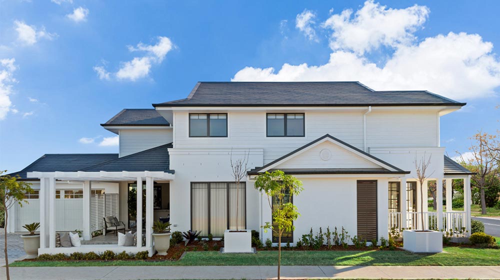 Modern white house with a black roof, front porch area, landscaped yard, and clear blue sky, showcasing contemporary residential architecture and outdoor design.