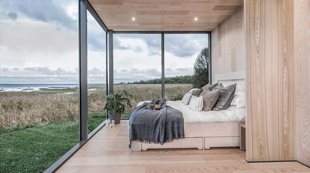 Bright bedroom with floor-to-ceiling windows showcasing scenic landscape, minimalist decor, and cozy bed with neutral tones, emphasizing natural light and tranquility.