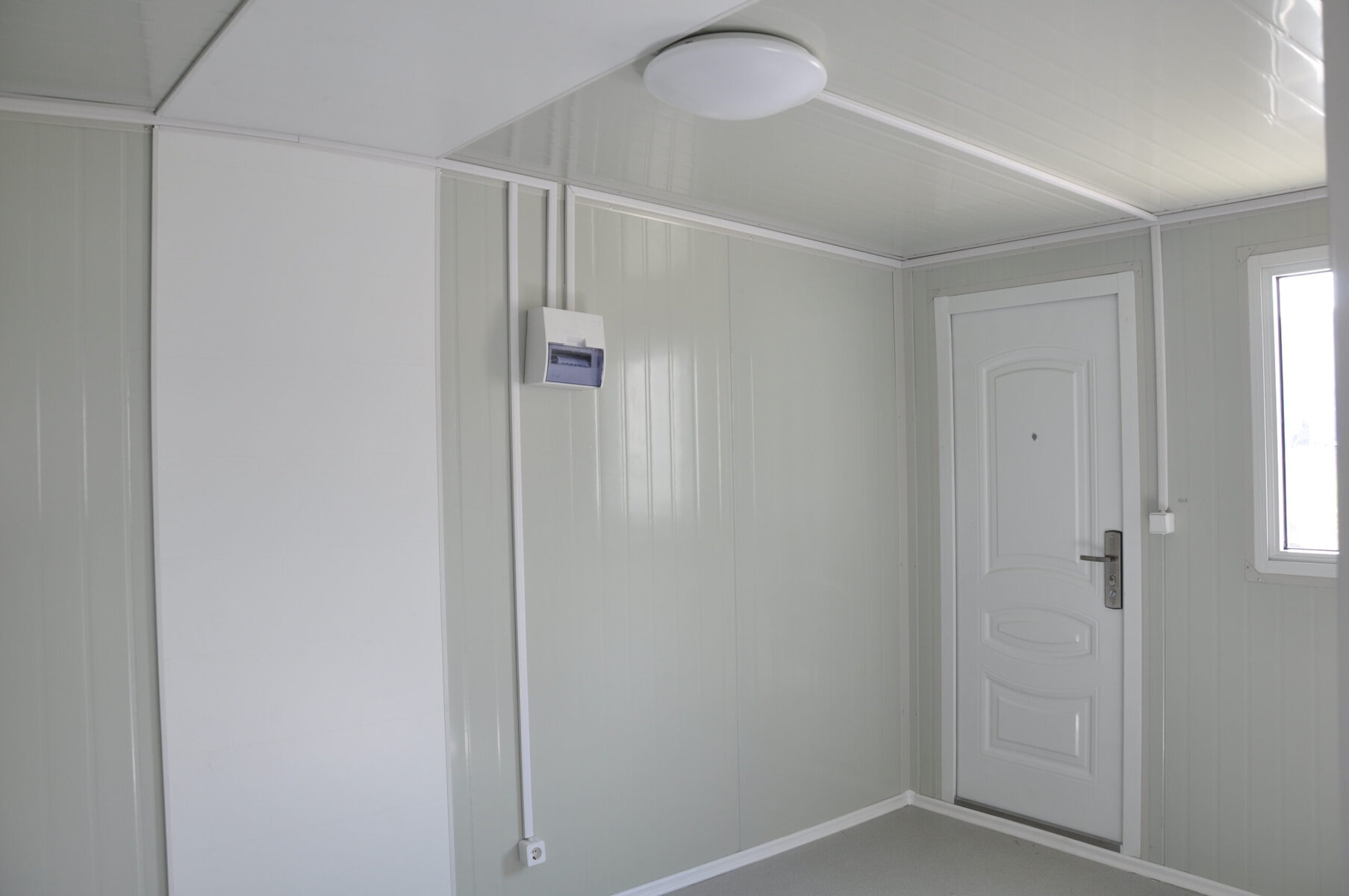 Clean white interior of a portable tiny house with seamless paneling, modern door, small window, and compact design, emphasizing Mobile Home, Portable Housing, Tiny Living, and Modern Interior keywords.