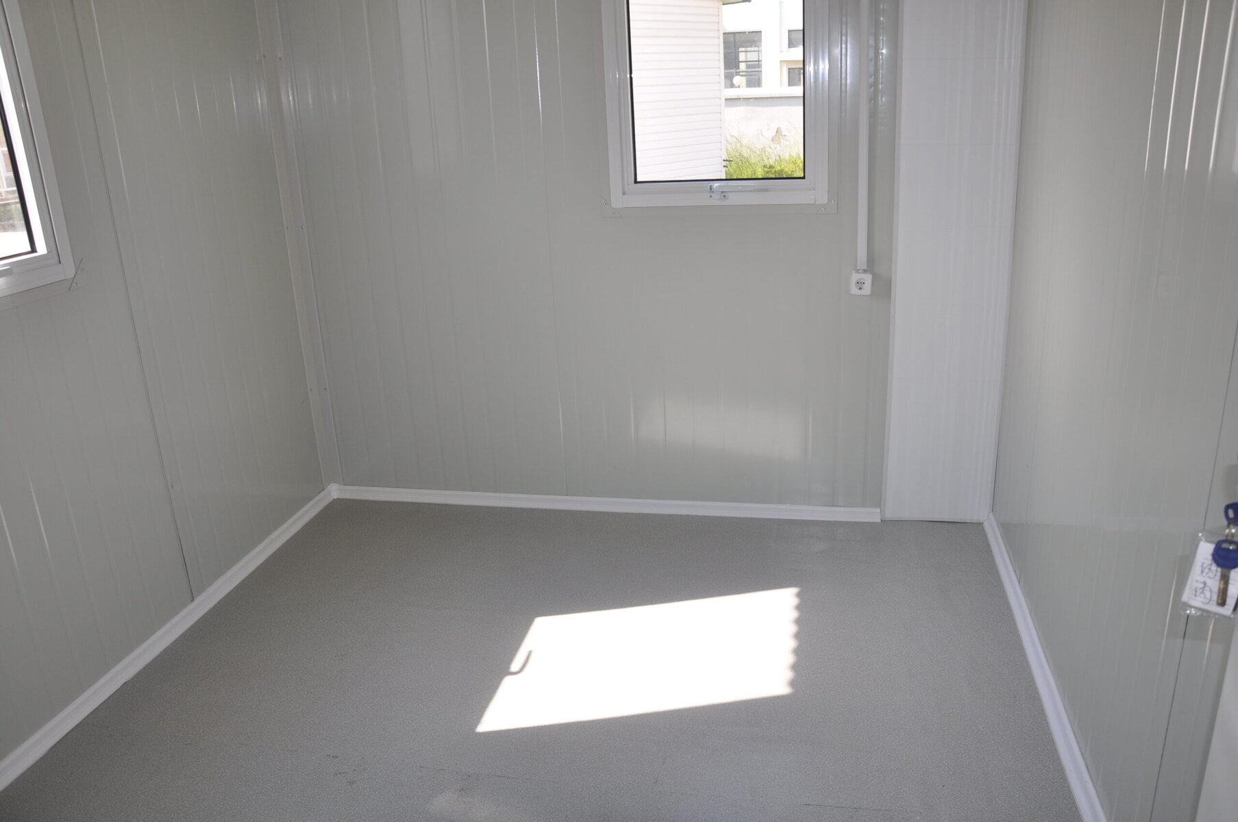 Modern insulated tiny house interior with light grey walls, white trim, and large windows providing natural light. Perfect for compact living or mobile homes with durable flooring and efficient design.