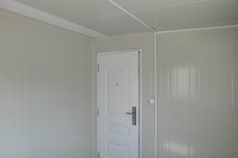 2. Interno pulito e isolato dell'ufficio portatile con porta bianca e pannelli murali verde chiaro, perfetto per cantieri edili o ambienti di lavoro remoti.