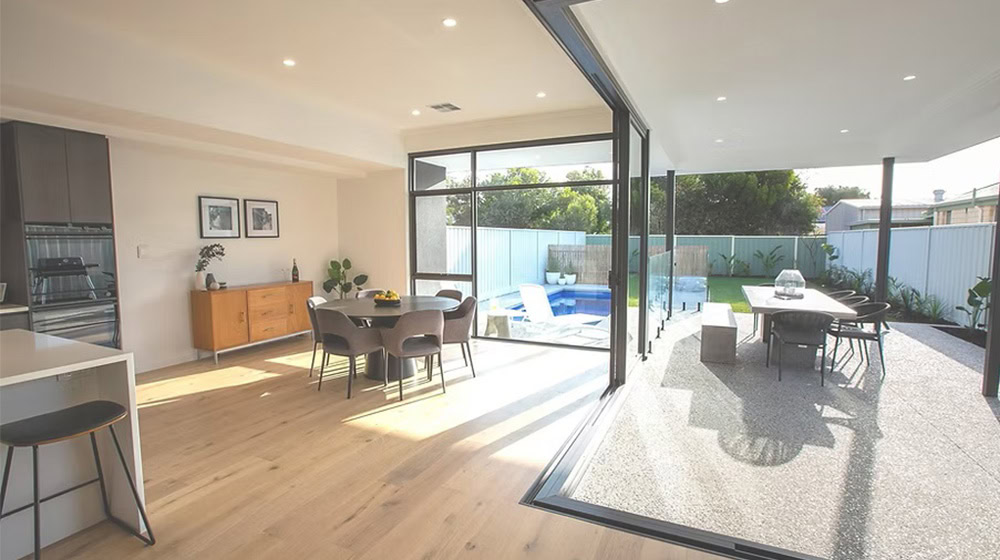 Bright open-concept living and dining area with seamless indoor-outdoor flow, featuring a modern glass sliding door that opens to a stylish outdoor patio and pool area.