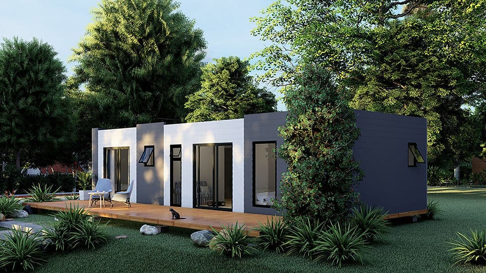 Modern single-story modular home with large windows and wooden deck, set among trees and greenery.