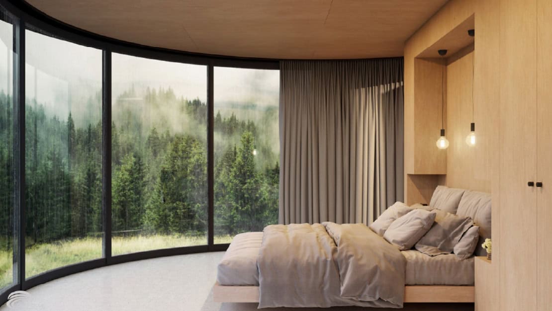 Modern bedroom with curved window, foggy forest view, neutral bedding, wood accents, and floor-to-ceiling curtains.
