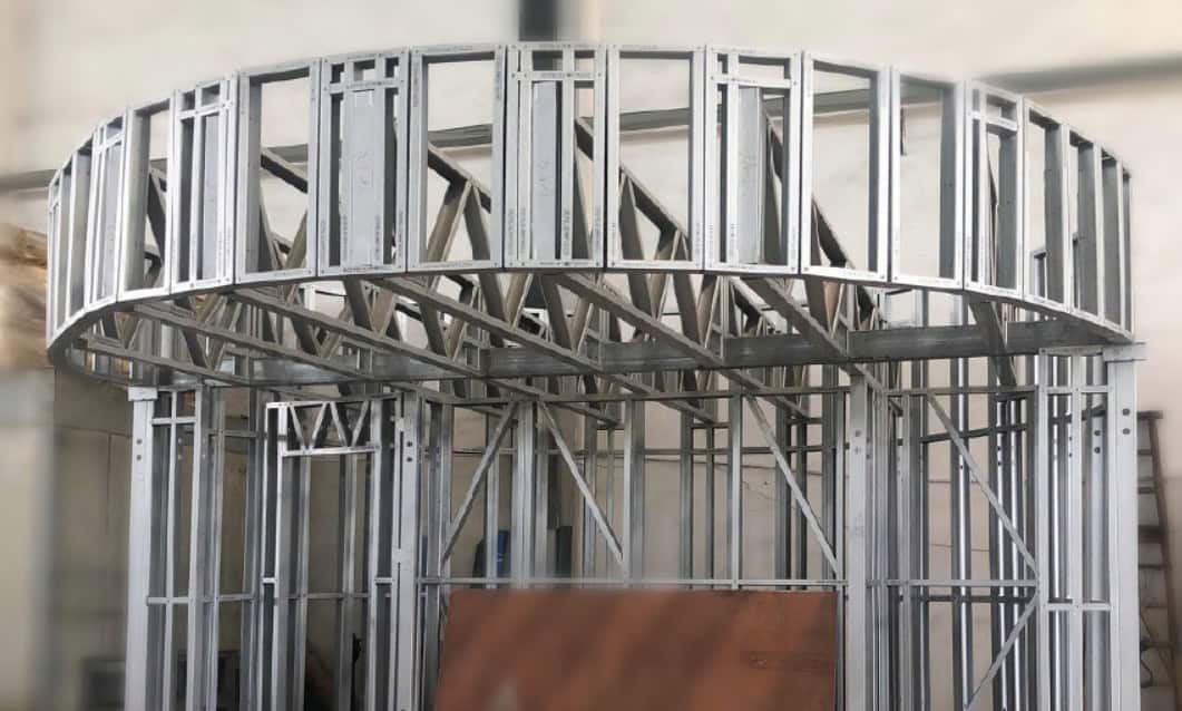 Circular metal stud frame with vertical and horizontal beams, indoors against a plain wall.