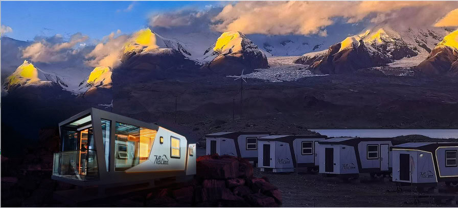 Modern modular cabins sit on rocky ground with snow-capped mountains and a glacier behind them under a partly cloudy sky.