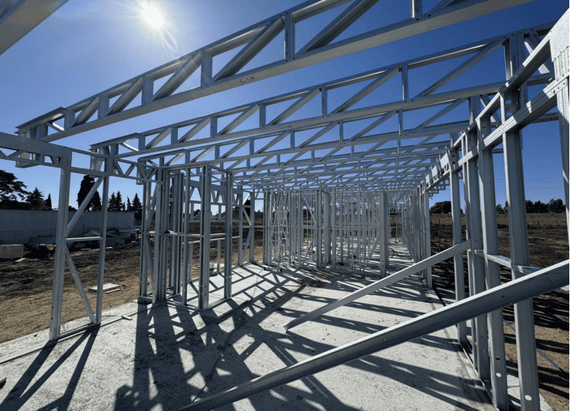 Steel building frame under construction, exposed beams and columns, sunlight casting shadows on concrete foundation.