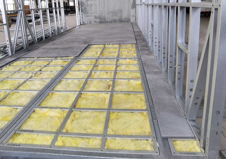 Under-construction building with exposed yellow insulation in floor and metal studs along the right wall.