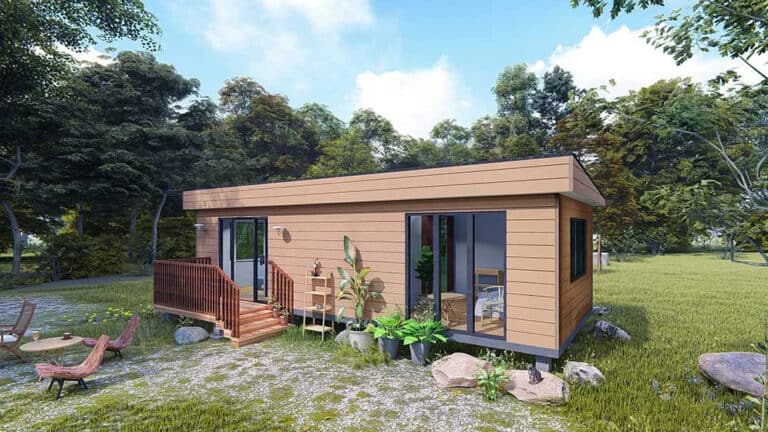 Modern tiny house with wood siding and big windows sits in a grassy clearing with trees and outdoor furniture.