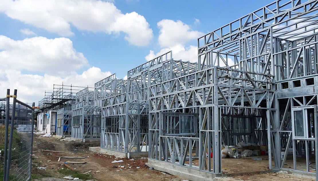 Partially built structures with exposed steel frames stand on a construction site beneath a partly cloudy sky.