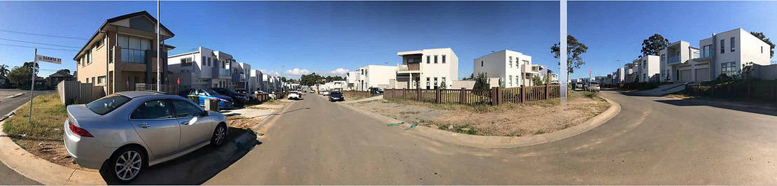 Suburban street with modern houses, parked cars, and a damaged car by the curb on the left.