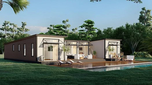 Modern modular home with large windows, wooden deck, lounge chairs, pool, and trees under a clear sky.