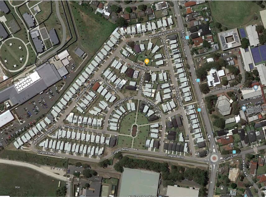 Aerial view of houses in a triangle street layout with green spaces; a nearby school is visible.