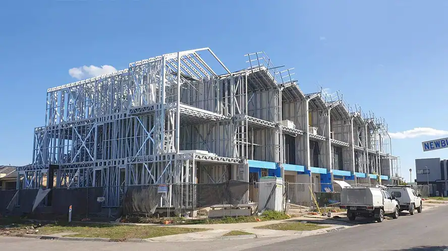 Steel frame of a multi-story building under construction, with vehicles and fencing visible on a clear day.