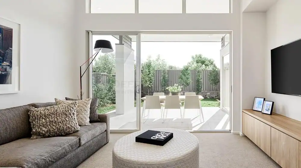 Modern living room with gray sofa, TV, and glass doors opening to a patio with table, chairs, and green backyard.