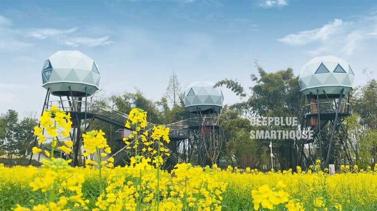 Three geodesic domes on stilts behind a yellow flower field, with trees and blue sky. "DEEPBLUE SMARTHOUSE" visible.