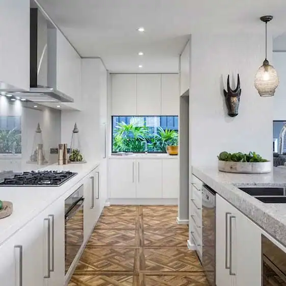 Modern galley kitchen with white cabinets, stainless appliances, wood floor, pendant light, and window facing green plants.
