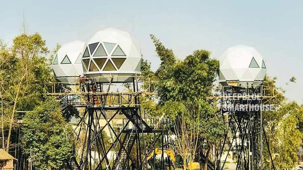 Three white geodesic domes on metal platforms among trees, set against a clear sky.
