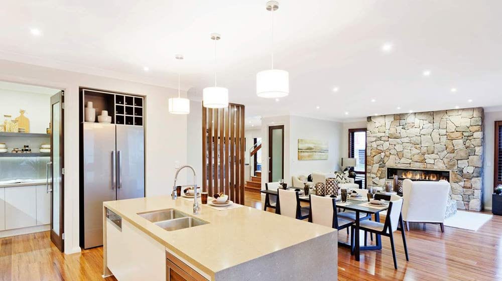 Open-plan kitchen, dining, and living area with stone fireplace, wood floors, pendant lights, and stainless appliances.