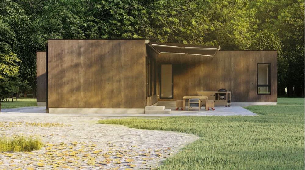 Modern wooden house on concrete foundation, with patio furniture and grill, surrounded by grass and trees.