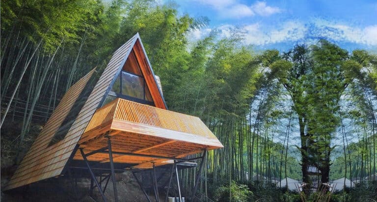 A modern A-frame cabin with a balcony stands on stilts amid dense bamboo under a blue sky.