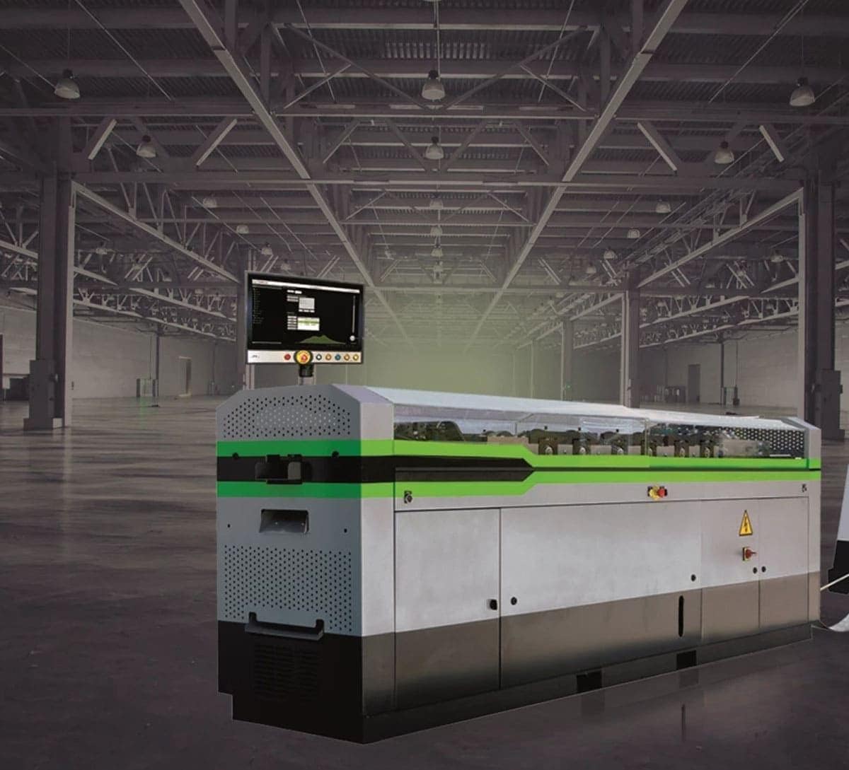 An industrial machine with a control screen sits in a spacious, empty warehouse with exposed beams and lighting.