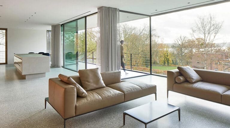 Luxury Bayonne villa: beige sofas, low table, large windows, person on balcony overlooking trees and houses.