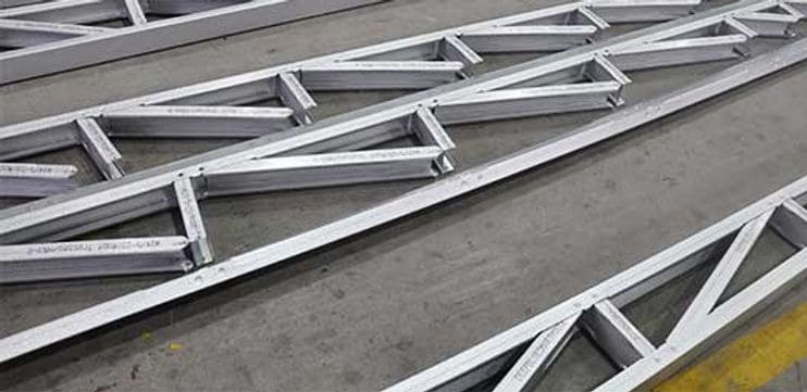 Metal trusses in parallel rows sit on a concrete floor, likely in an industrial or construction area.