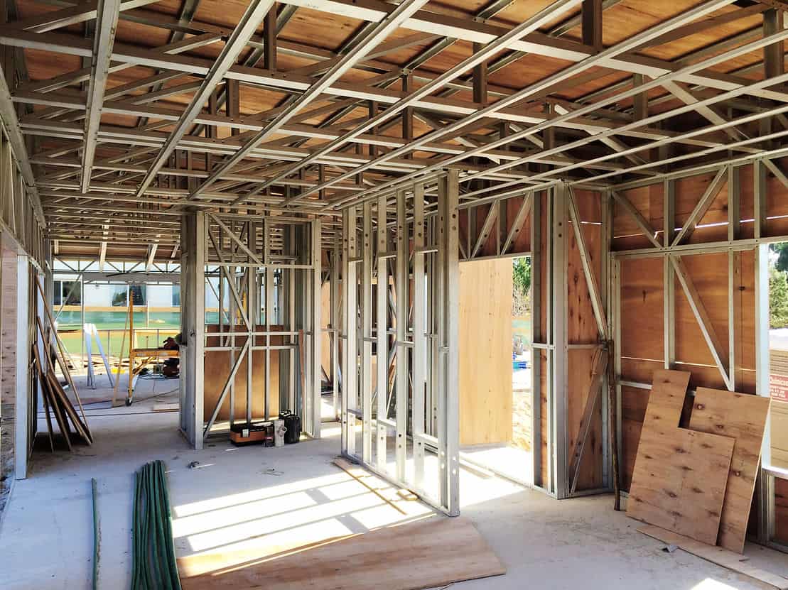 Building interior under construction with exposed metal framing, plywood panels, and materials scattered on the floor.