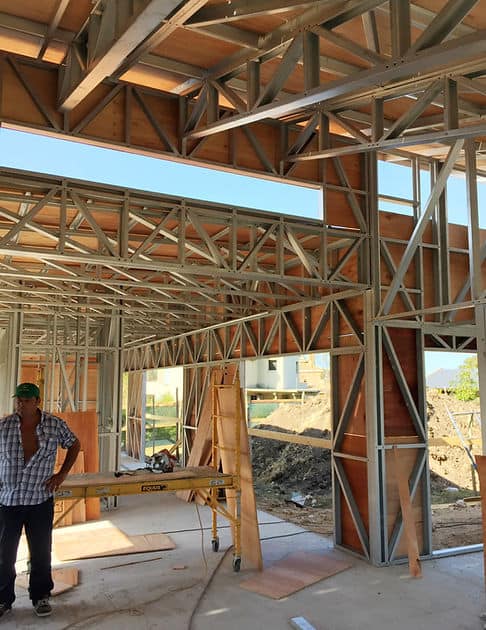 A building under construction with steel frames and wood panels; a person stands by a worktable inside.