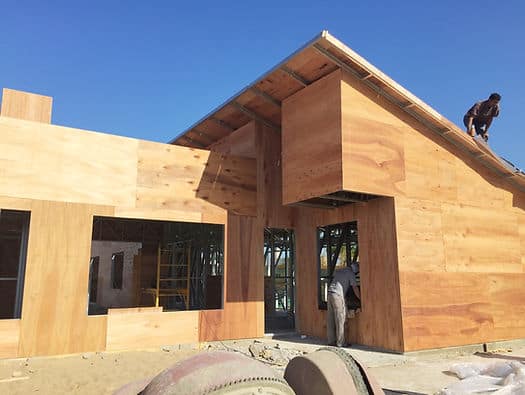 Partially built wooden building; one worker on the roof, another under a covered entrance.