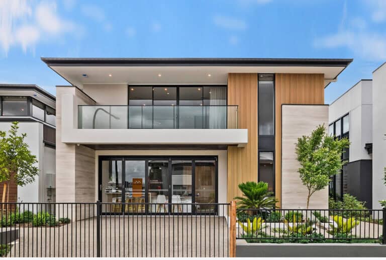 Modern two-story house with large windows, balcony, wood accents, landscaped yard, and black metal fence.