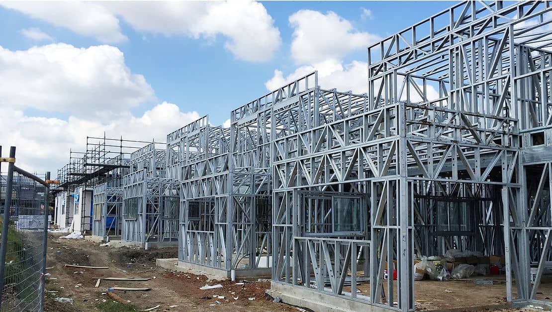 Partially built structures with exposed steel frames and scaffolding beneath a partly cloudy sky.