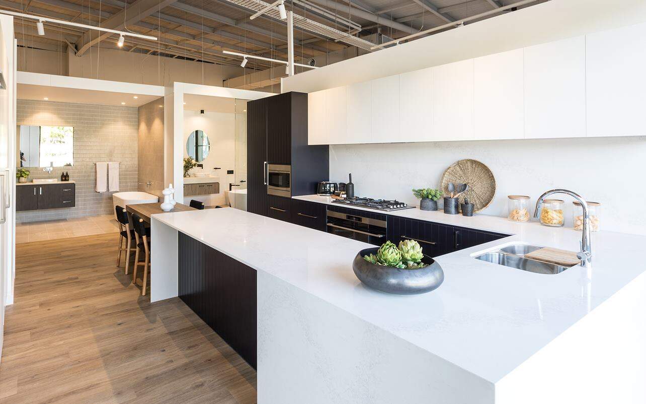 Modern kitchen with white counters, black cabinets, oven, cooktop, plants; open dining area and bathroom in background.