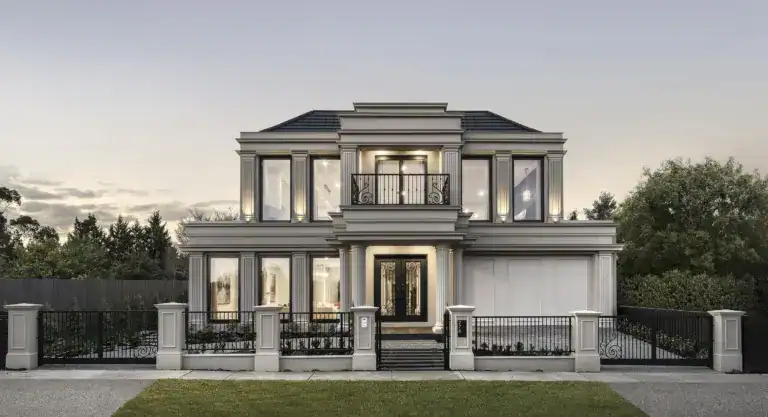 Modern two-story mansion with large windows, beige walls, black roof, and iron fence seen from the lawn at dusk.
