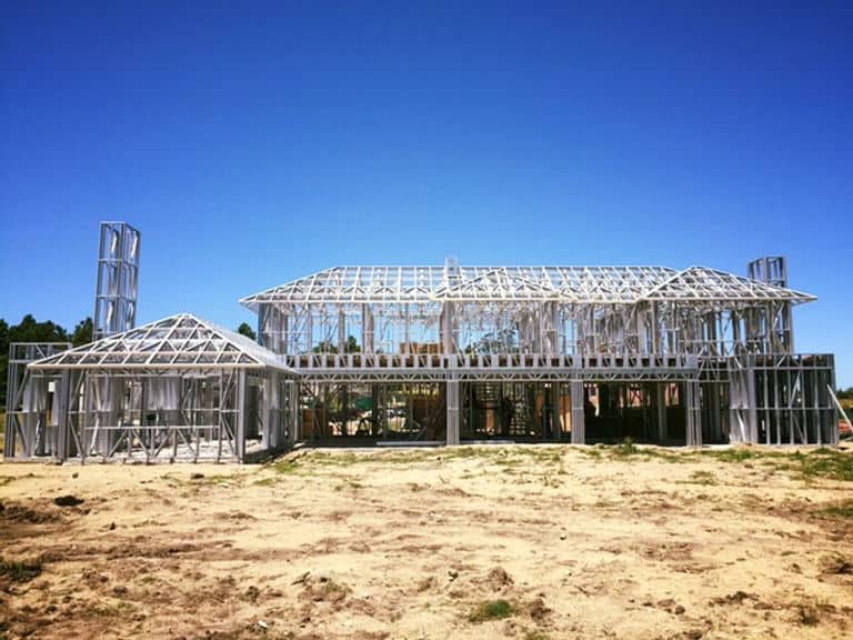 Steel building frame under construction on a dirt lot with a clear blue sky in the background.
