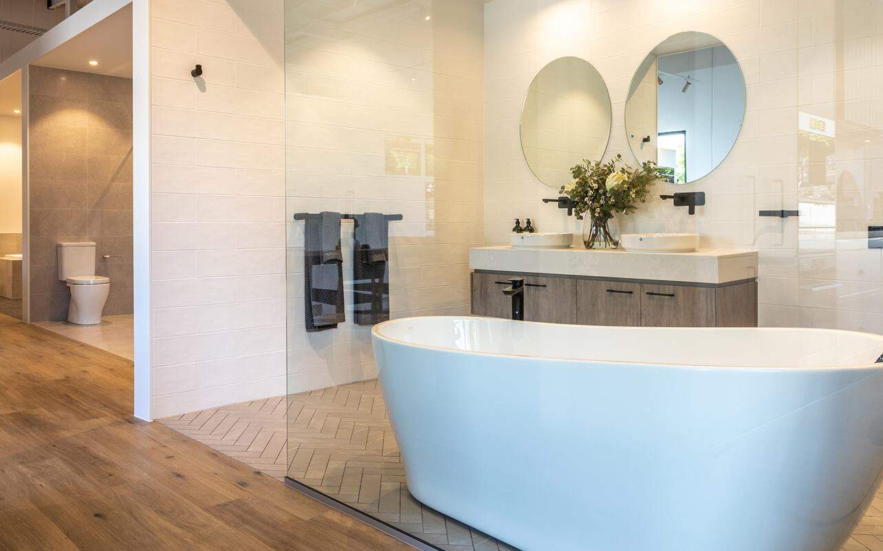Modern bathroom with freestanding tub, double vanity, two round mirrors, wood floor, and a separate toilet area.