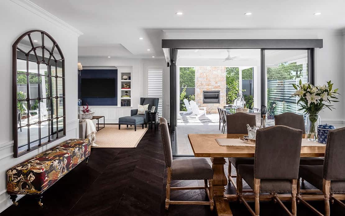 Open-plan living and dining area with a wooden table, mirror, and sliding doors to a patio with fireplace.