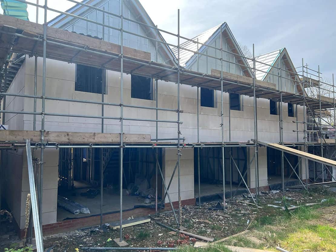 Partially built houses with scaffolding, open windows, and scattered building materials on the ground.