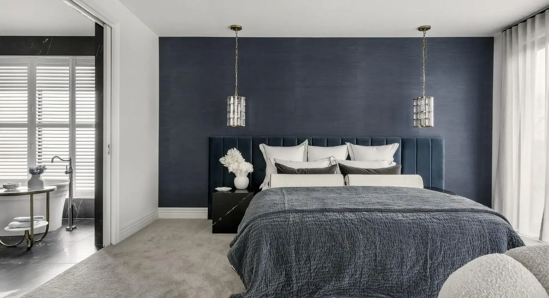 Bedroom with navy accent wall, upholstered headboard, pendant lights, and open door to adjoining bathroom.