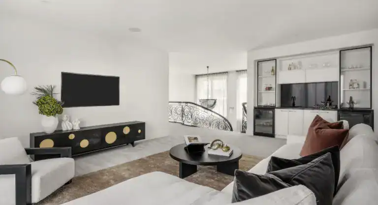 Modern living room with a sectional sofa, coffee table, wall TV, built-in bar, and staircase with ornate railing.