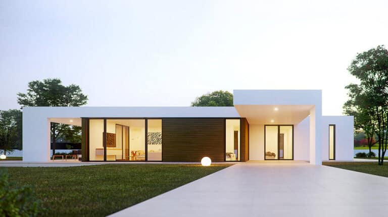 Single-story modern house with large windows, flat roof, white and wood exterior, on a lawn at dusk.
