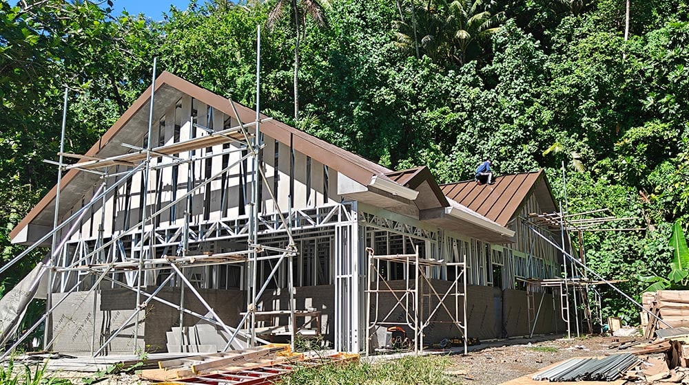 Modern house under construction with scaffolding in lush green environment, showcasing contemporary building design and sustainable architecture.