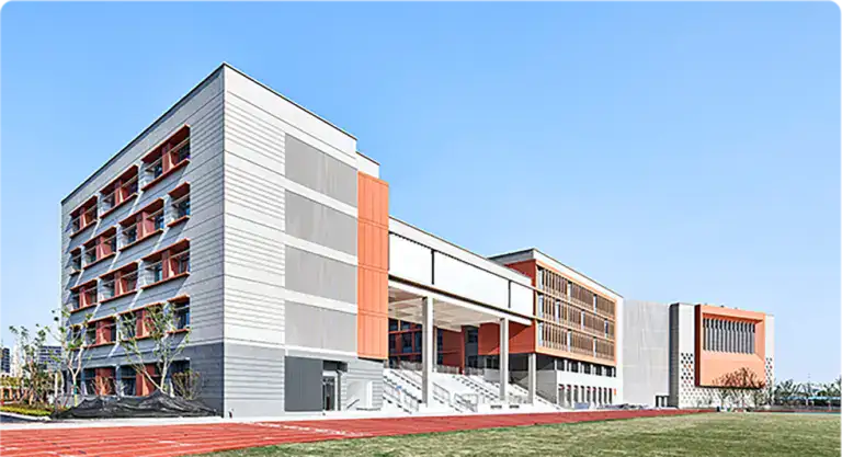 Modern university building with sleek design and clean lines, featuring large windows and an open walkway, under a clear blue sky.