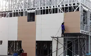 Modern building under construction with scaffolding and workers installing exterior panels, showcasing innovative architectural design and construction techniques for commercial or residential projects.