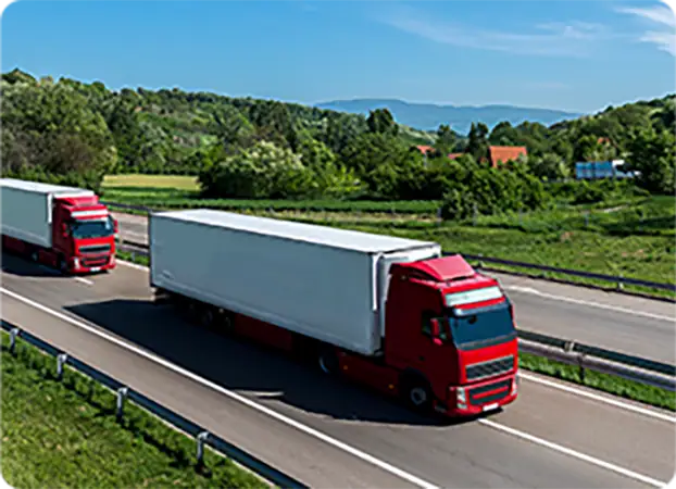 Semi-trucks driving on a highway with green landscape in the background, representing logistics and transportation.